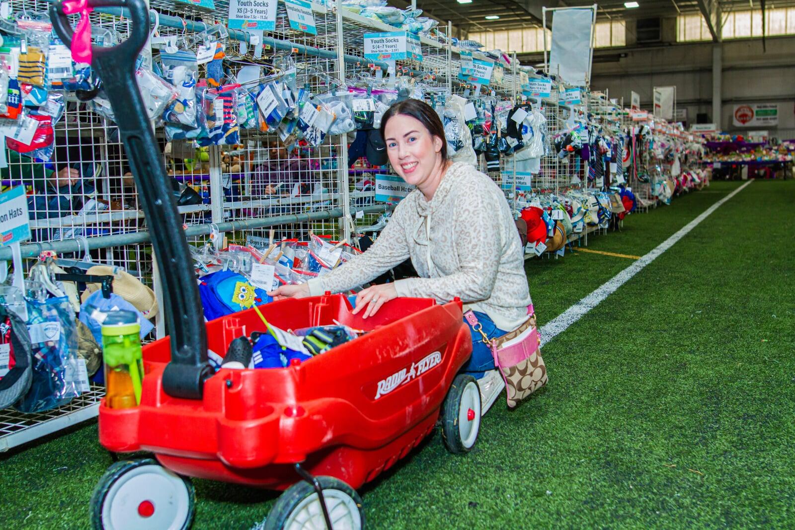 Woman sitting on the astro turf putting items in her red wagon.