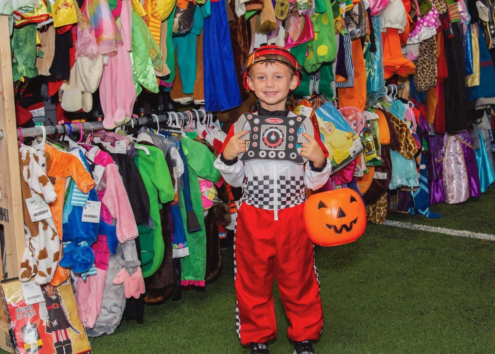 Boy in a halloween costume holding an orange plastic pumpkin.