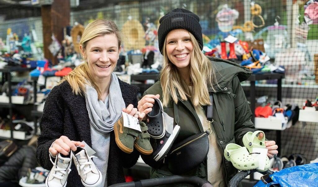 Two woman smile as they hold up shoes.