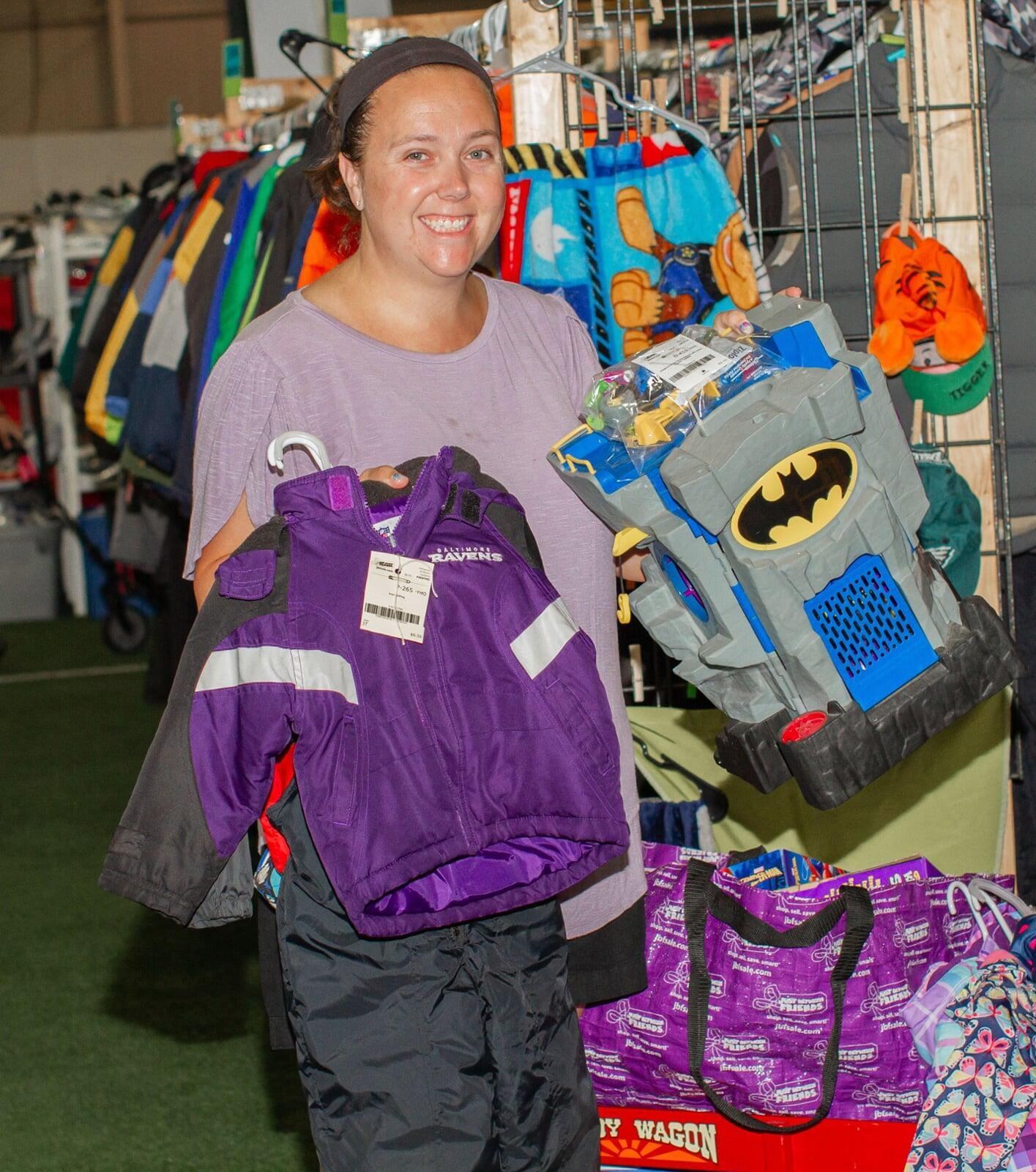 Smiling woman holding up a batman toy and a purple and black jacket