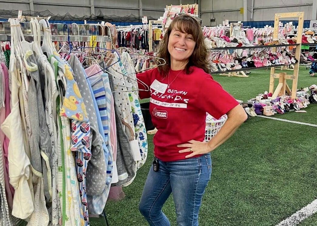 A JBF Team Member wears a black JBF apron while organizing infant clothing on the clothing racks.