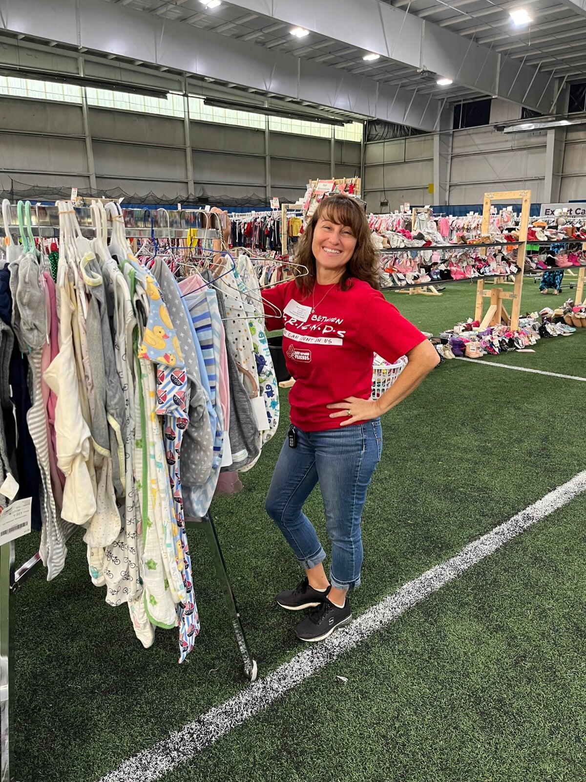A JBF Team Member wears a black JBF apron while organizing infant clothing on the clothing racks.