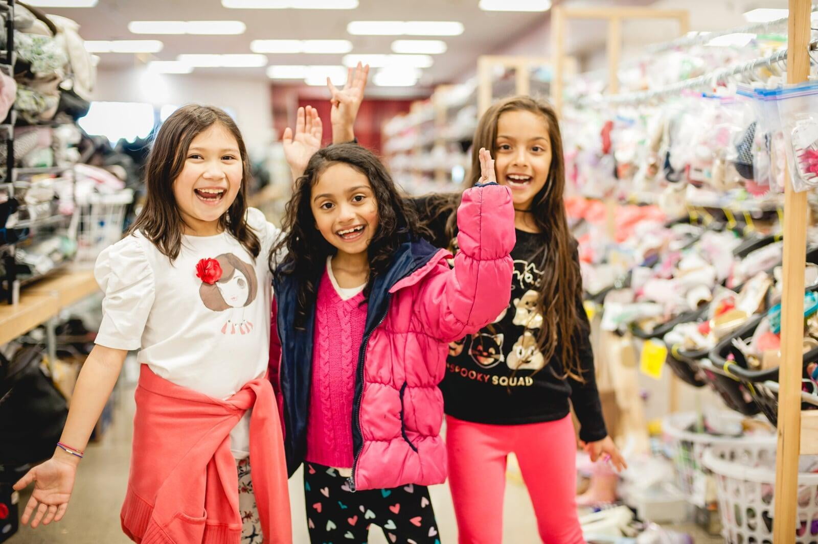 Three young girls are excited to shop together in the toy section of their local JBF sale.